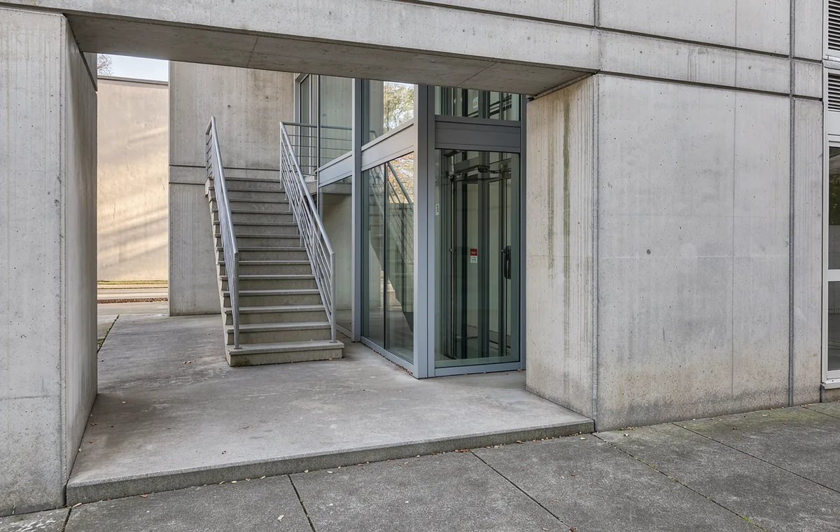 A rectangular opening in a pale apartment building reveals an exterior stair and a sunlit courtyard wall